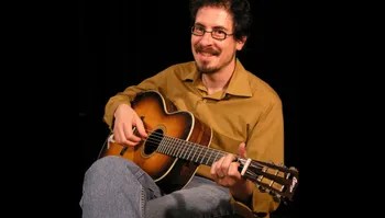 photograph of david hamburger smiling while playing an acoustic guitar