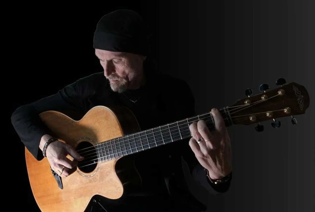 Dylan Fowler playing guitar in the shadows of a black background