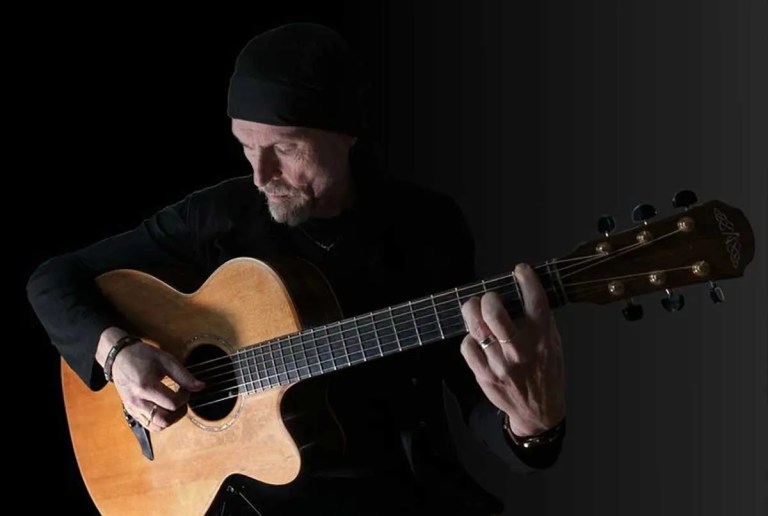 Dylan Fowler playing guitar in the shadows of a black background