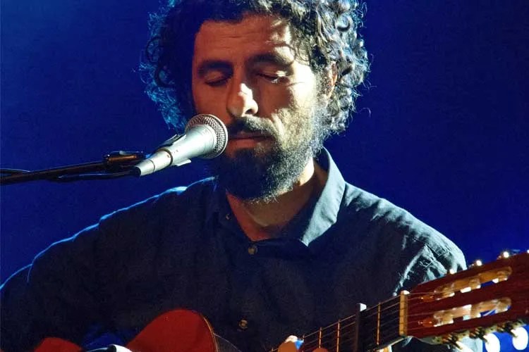 singer-songwriter José González sings into a microphone while holding an acoustic guitar