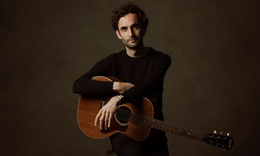 Julian Lage seated with guitar. Photo by Alysse Gafkjen