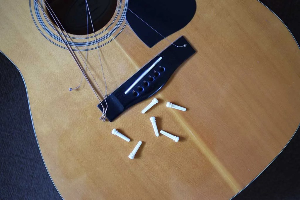loose guitar strings on soundboard with bridge pins pulled from bridge