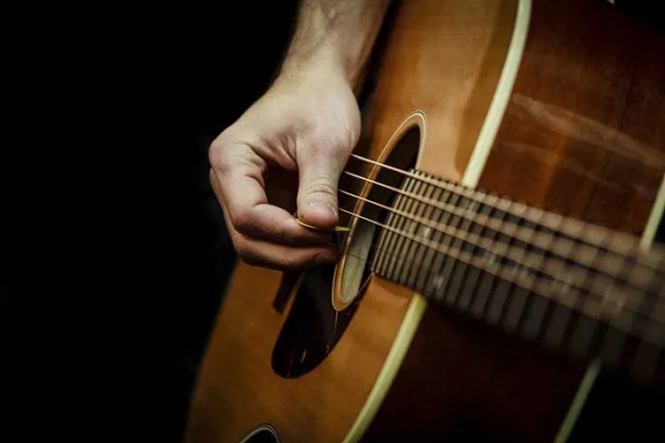 closeup of a hand holding a pick and strumming an acoustic guitar