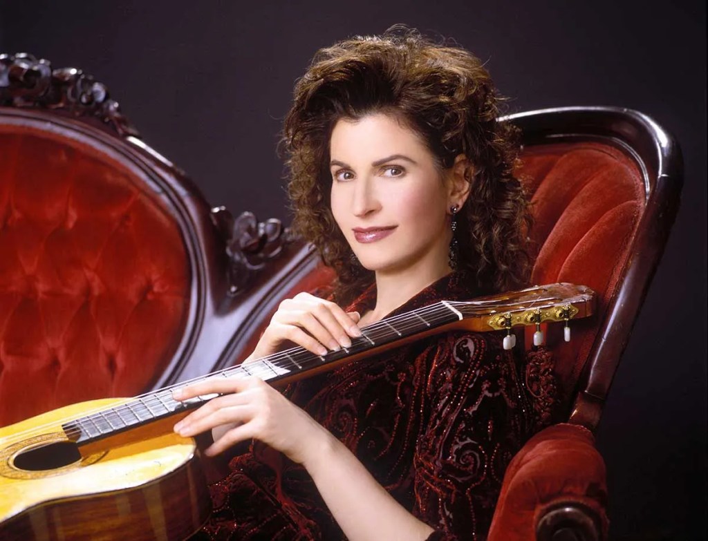 Sharon Isbin reclining on red velvet couch with acoustic guitar, Photo: J. Henry Fair